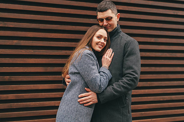 Couple embraces affectionately while posing against a wooden wall in a cozy urban setting during autumn