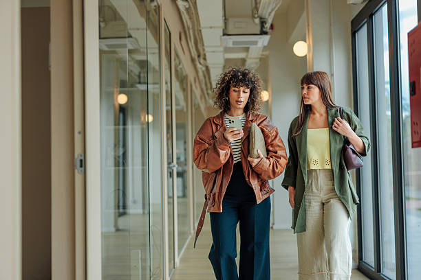Two businesswomen walking and talking in office hallway