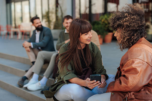 istock Young women talking and using a smartphone outdoors with colleagues in the background 2221031649
