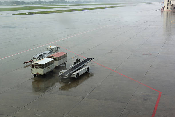 istock Truck with trailers for transportation luggages.Preparing a conveyor belt trailer for aircraft luggage loading or unloading in airport during rainy weather conditions 2221037556