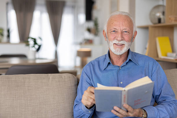 istock Smiling old man reading happily on the couch 2221050722