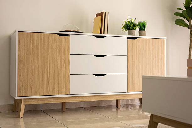 A simple living room showcasing a sideboard cabinet, ceramic tile flooring, and a white wall background.