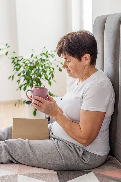 istock Senior woman enjoying hot drink and reading book 2221055270