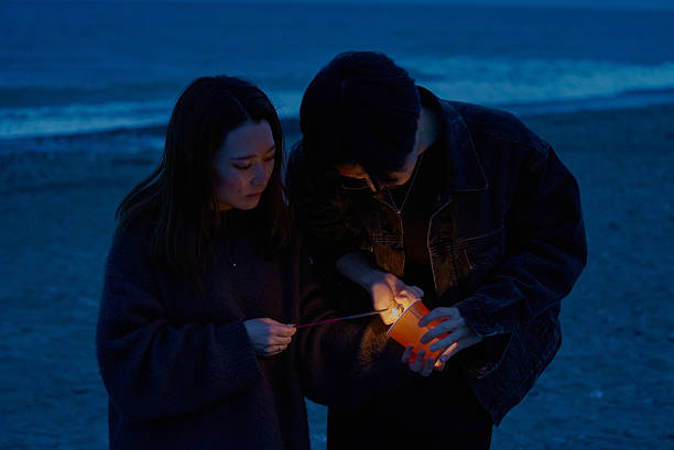 Young man and woman playing hand-held fireworks on the beach at night