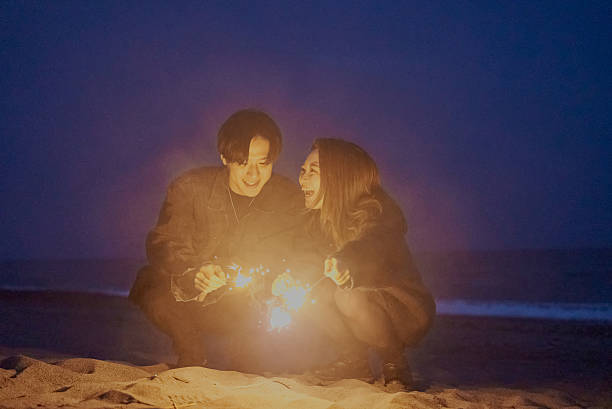 istock Young man and woman playing hand-held fireworks on the beach 2221057300