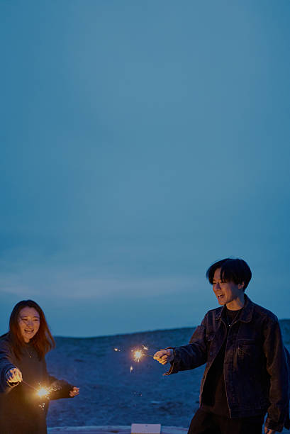 Young man and woman playing hand-held fireworks on the beach