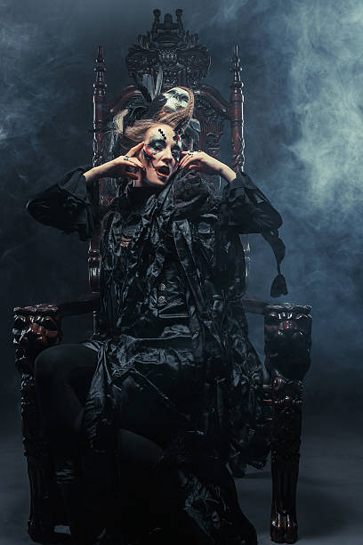 istock Young beautiful witch sits on a chair. Bright make up, skull, smoke-  halloween theme. 2221058568