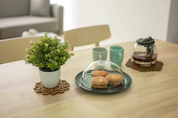A tea party table with a coffee pot, cups, and cupcake pieces on a wooden dining table.