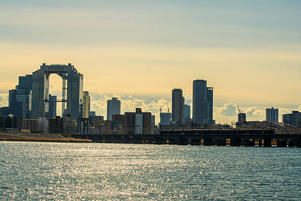 Osaka, Japan - December 11, 2024: Hankyu Railway train across Yodogawa river with beautiful view of umeda sky building and city at sunset. Famous travel destination for observation deck.