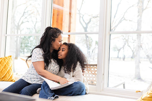 istock Mother lovingly kisses daughter's forehead by window 2221063157