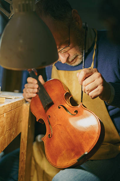 istock Skilled craftsman carefully restoring vintage violin, using precision tools while focusing on intricate details of instrument's structural integrity and acoustic performance 2221064525