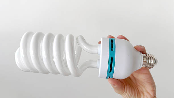 istock Hand holding a large spiral compact fluorescent light bulb (CFL) with E27 base on white background. Energy-saving eco-friendly daylight lamp detail close-up 2221066510