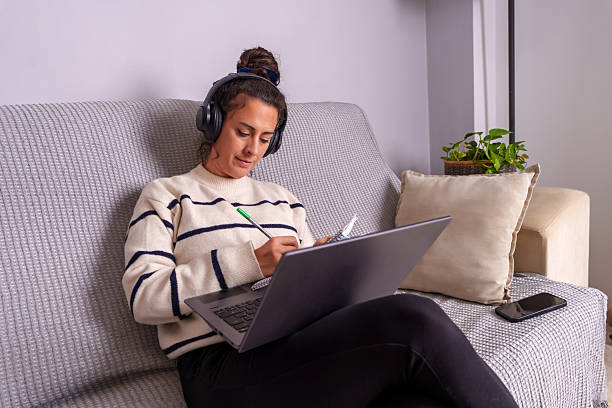 istock Focused young woman taking notes while attending online course from home 2221074454