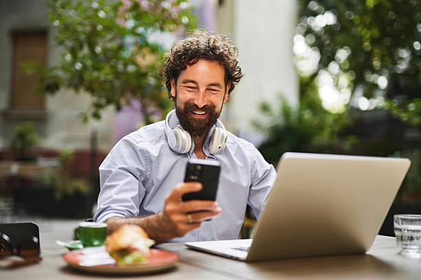 Happy businessman working remotely at a cafe, using laptop and smartphone