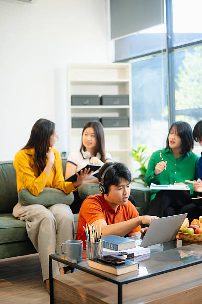 istock Group of young Asian students working on a project with laptops and tablets. Cozy indoor setting, teamwork, 2221078758