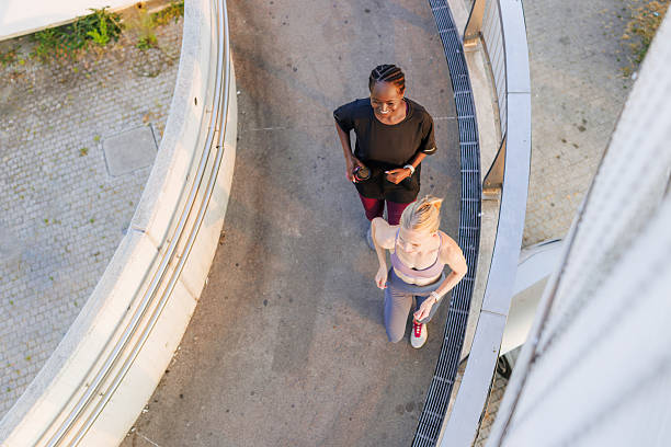 Two active women are jogging along a curving path, enjoying outdoor fitness and healthy lifestyles. The aerial perspective highlights their movement, companionship, and dedication to staying fit in a natural environment.
