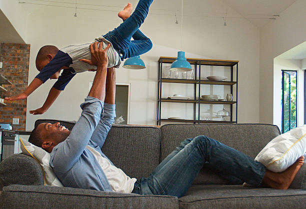 istock Father Lying On Sofa At Home Having Fun With Son Lifting Him Into The Air 2221095545