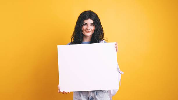 istock Smiling student showing white blank board on yellow background 2221104132