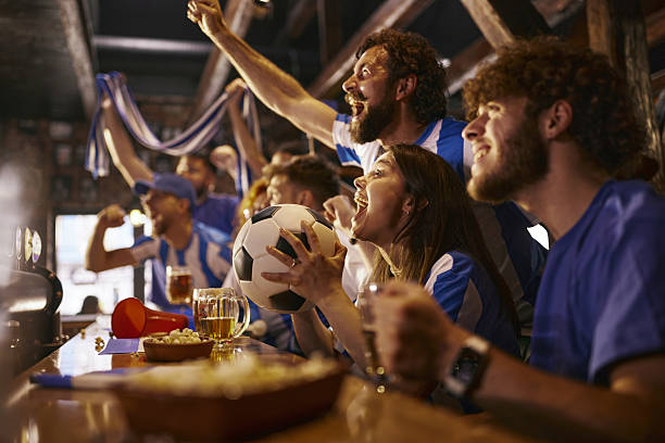 istock Excited soccer fans cheering while watching a match on TV in a pub. 2221105235