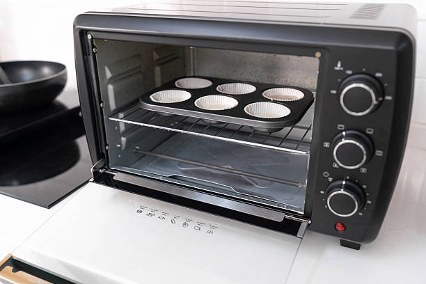 Six-slot muffin tray with batter in a black toaster oven on white kitchen counter