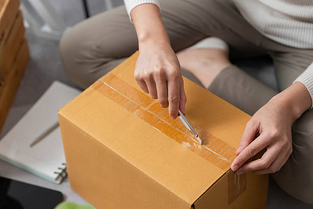 istock Moving tasks. Woman using a utility knife to open a delivery box. 2221112622