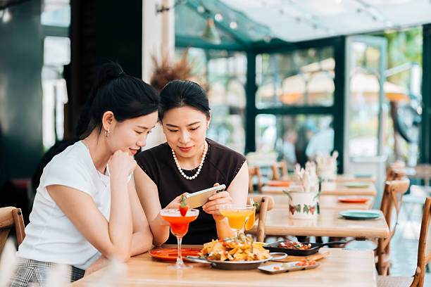 istock Two young Asian women using smart phone while having lunch together in restaurant. Luxury lifestyle. Enjoying life with good food. People, food, lifestyle and technology. 2221114462