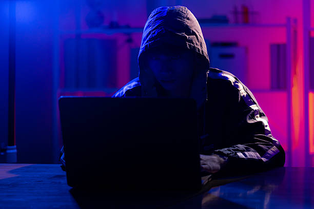 istock Young Man in Hoodie Working on Laptop in Dark Tech Environment 2221118433