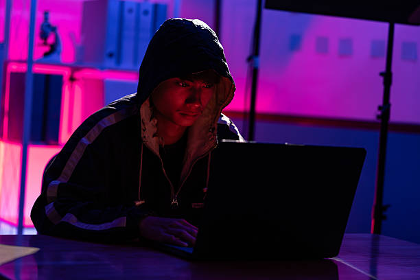 istock Young Man in Hoodie Working on Laptop in Dark Tech Environment 2221118434