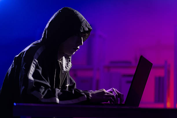 Young Man in Hoodie Working on Laptop in Dark Tech Environment