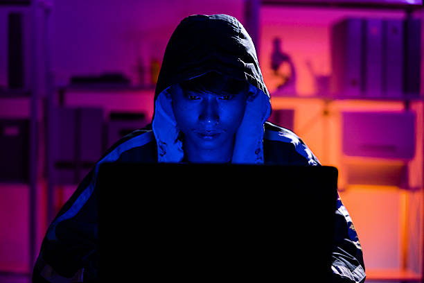 istock Young Man in Hoodie Working on Laptop in Dark Tech Environment 2221118439