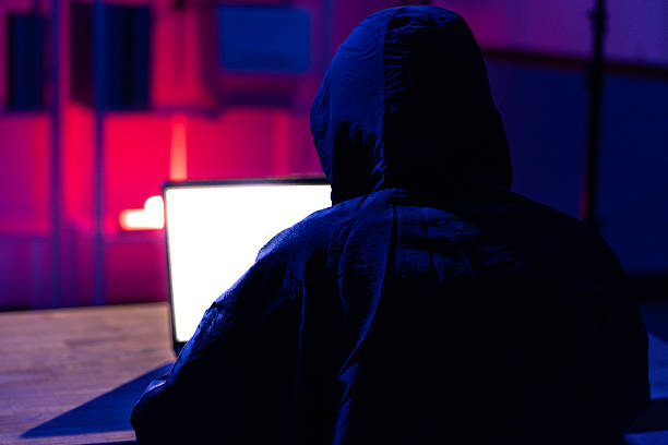 istock Young Man in Hoodie Working on Laptop in Dark Tech Environment 2221118446