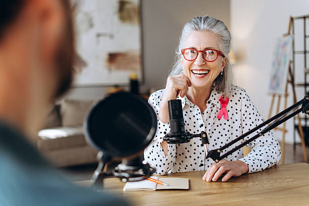 istock Senior podcaster wearing pink ribbon talking into microphone 2221119521