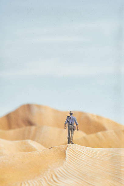 The sun beats down on a miniature adventurer as he crosses the sand dunes in an arid desert. Scale model photography.
