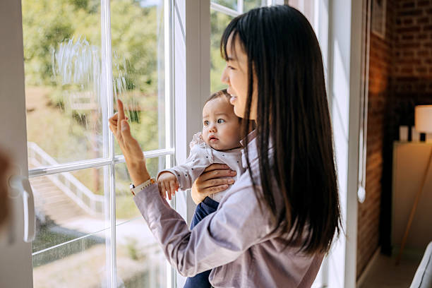 istock Woman holding baby girl while checking dirty window with concern 2221141401