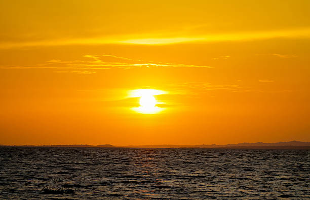 istock Solar eclipse at sunset across the sky above the sea. Red orange sunset light 2221144173