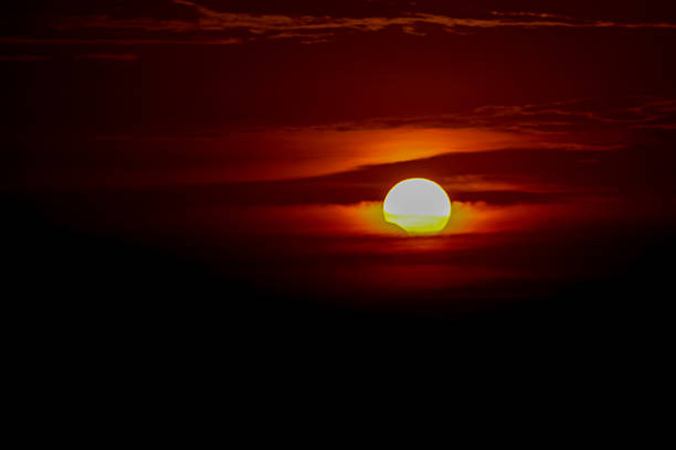 Solar eclipse at sunset across the sky above the sea. Red orange sunset light. Solar eclipse at sunset. Sunset light across the sky between the clouds