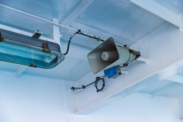 Close-up image of a ferry boat's intercom speaker and fluorescent light fixture mounted on the interior ceiling. The photo captures the utilitarian design and wear of maritime equipment, showcasing exposed wires, rust, and weathered surfaces, typical for working vessels. Taken on a ferry in Croatia during a sunny summer day, the image provides a raw, documentary-style view ideal for industrial, transport, or nautical-related content.