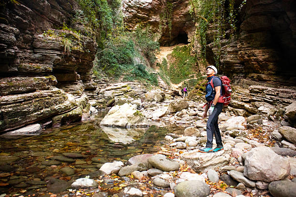 Marche, Italy: a man equipped with a helmet and backpack hiking along the river in the Garrafo Canyon (Gole del Garrafo). Other two hikers, a man and a woman, are in the background