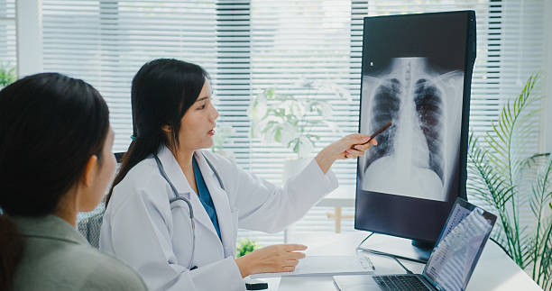 istock Young Asian female doctor analyzing lung X-ray and explaining diagnosis to patient during consultation in modern medical clinic office. 2221152246