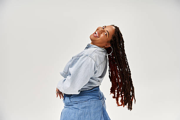 istock Confident woman with braids poses in denim attire against a soft grey backdrop 2221153543