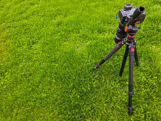 Camera sits on tripod in peaceful grassy field under clear blue sky. Natural light enhances tranquil outdoor setting, inviting exploration and creativity.