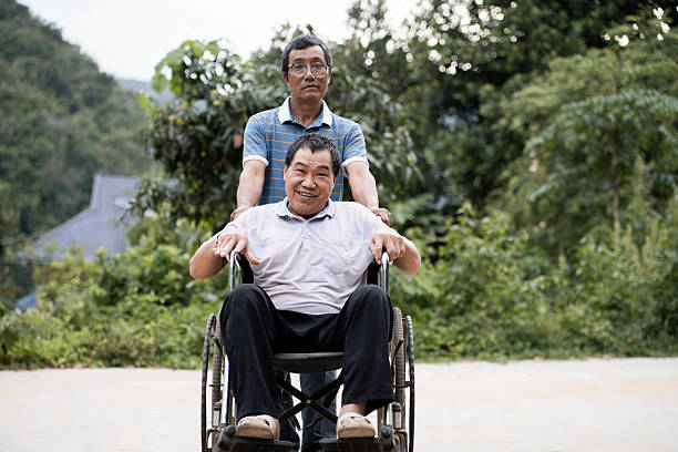 A cheerful elderly man in a wheelchair shares a fist pump and smile while family members walk beside him in a park showcasing inclusion care and support