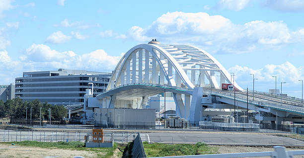 Osaka, Japan - April 15, 2025: Looking northeast to Yumemai Bridge connecting Yumeshima Island in the foreground and Maishima Island in the background. This route leads to the West Gate of EXPO 2025 OSAKA and the industrial district by Osaka Bay. Buildings in Hokkushiratsu district stand in the background. Spring morning in Konohana Ward.