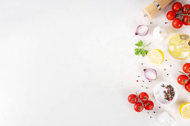Spices, black pepper, garlic, onion, greens and tomatoes, olive oil on white cooking table. Ingredients for cooking food on the white stone concrete background top view copy space.