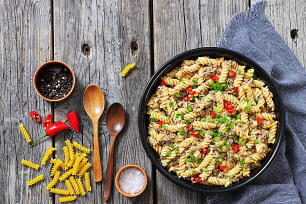creamy ground beef pasta, cheeseburger fusilli pasta sprinkled with green onion and chili pepper in a bowl on rustic grey wood table with spoons and ingredients, flat lay, not AI generated