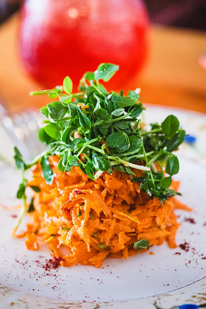 Vertical close-up of shredded carrot salad topped with microgreens, photographed in natural indoor light with a softly blurred background.