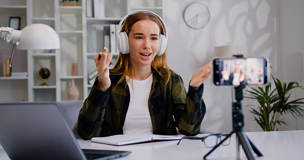 istock Young woman is live streaming a training blog at home. Chat online with channel subscribers. Blogger writes a video blog using a smartphone. 2221189303