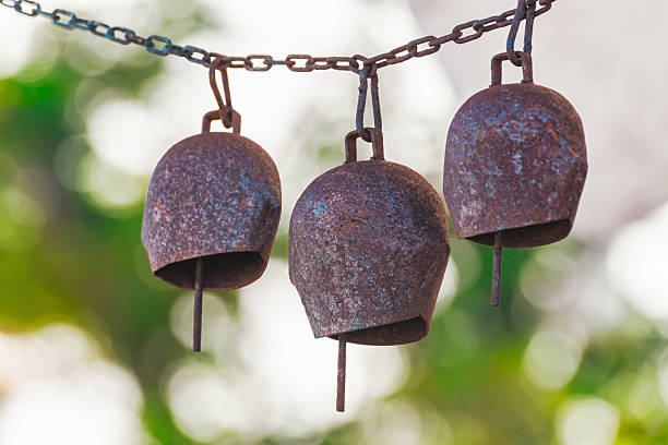 istock Rusty iron bells hanging on a chain with blurred green background, rustic outdoor decor 2221210058