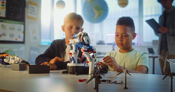 Elementary School Students Studying Model of Innovative Robotic Arm During Science and Engineering Lesson. Diverse Smart Young Boys Sitting at Table in Group in Classroom. Interactive STEM Education.