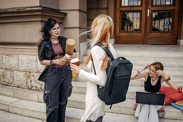 Friends enjoying together after class in front of university standing on stairs while having coffee